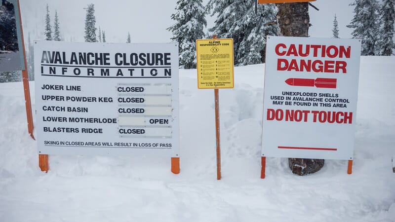An image of two outdoor signs in the snow warning of an avalanche and the shells used to control it.